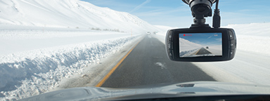 dashcam mounted behind a windshield driving on a clear road with a snow-covered landscape