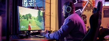 game thủ ngồi ở bàn máy tính ở nhà, trên màn hình là trò bắn nhau PVP
