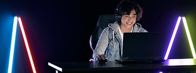 Seorang gamer muda bermain di laptopnya dalam ruangan yang gelap