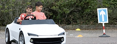 2 bambini sorridono mentre guidano un'auto bianca in miniatura della scuola guida Young Driver