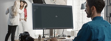 照片编辑在工作室的台式电脑前工作，显示器上显示着 Photoshop 正在加载