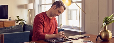 A man at home sitting at a table, installing an SSD into his open laptop with tools nearby