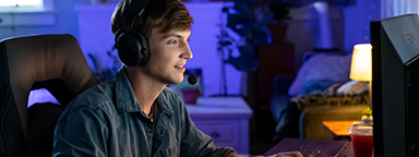 Młody mężczyzna grający w zaciemnionym pokoju na komputerze.