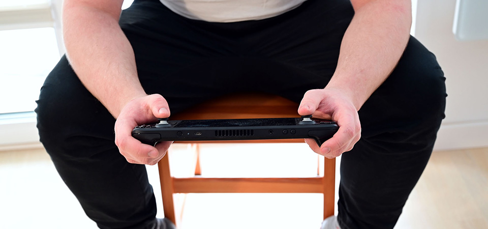 Installing a new SSD in a Steam Deck is only half the battle: making sure it has the right version of the Steam OS is just as essential. A gamer sits on a chair in a bright room and plays on a Steam Deck.