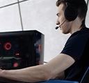 一名年轻男子坐在桌前的游戏椅上，在台式机上玩网络视频游戏