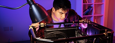 Młody mężczyzna zaglądający do otwartej obudowy komputera stacjonarnego na biurku, który zamierza złożyć nowy komputer do gier