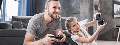 тато і донька сидять на ковдрі в кімнаті та грають у відеогру