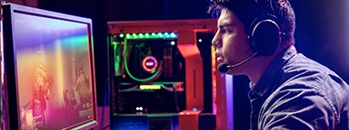 一名年轻游戏玩家坐在桌前带着耳机玩 PC FPS 游戏，背景中包含他的电脑桌面