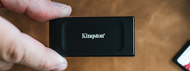 茶色の背景に Kingston XS1000 外付け SSD を持つ手。