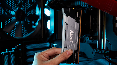 Una mano sostiene un módulo Kingston FURY Renegade DDR4 RGB dentro de una elegante carcasa de computadora negra y roja.