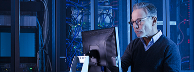 Due persone in piedi in un futuristico data center mentre esaminano insieme il monitor di un laptop