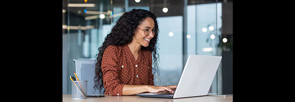 A smiling woman works on a laptop at a desk