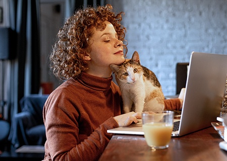 mujer trabajando en un portátil desde casa con un gato en su escritorio