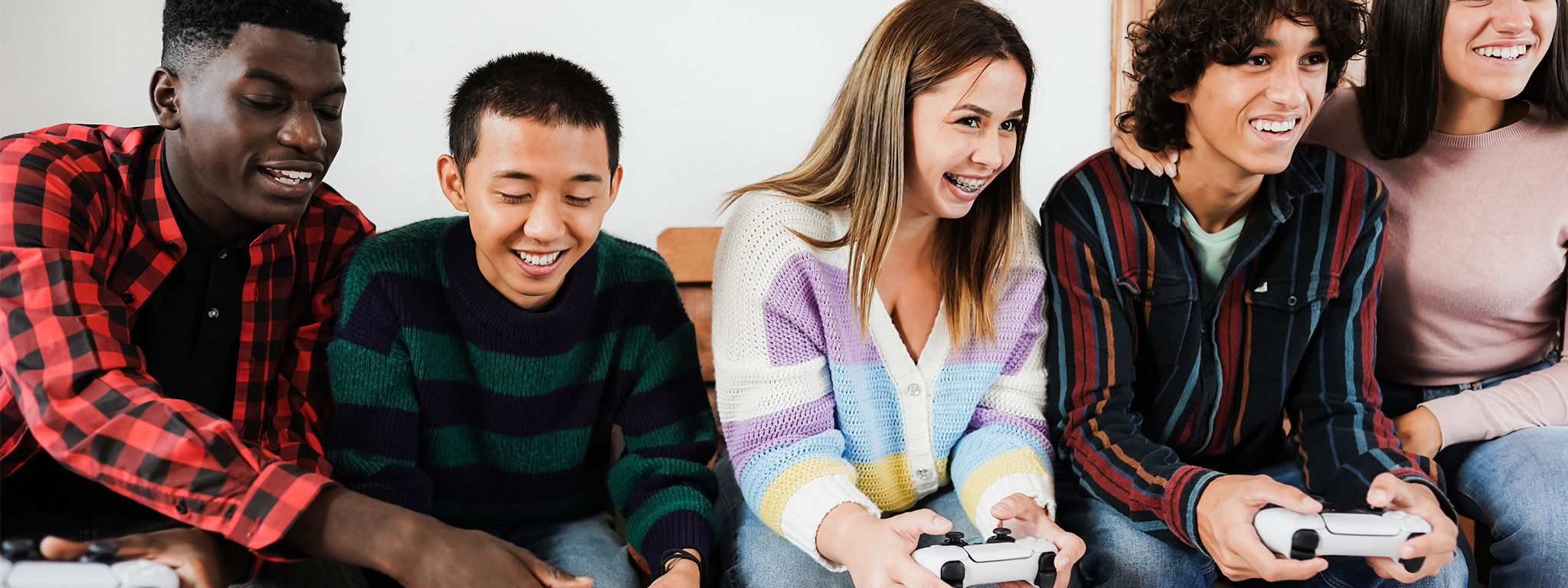 Cinco jugadores en un sofá en casa, cuatro jugando con mandos de PS5.