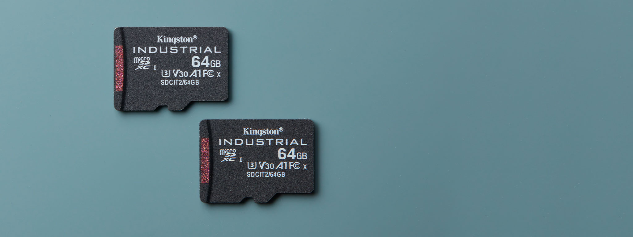 Пара карт пам’яті Industrial microSD ємністю 64 ГБ лежить на синьо-зеленій поверхні