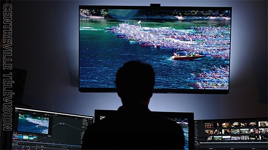 Silueta de un editor de vídeos trabajando con monitores y una pantalla más grande que muestra su proyecto en una habitación poco iluminada